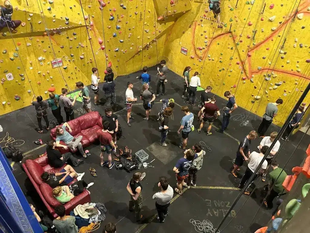 Overhead Inside Dynamic Rock Bouldering Gym With a Crowd of People on the Floor Getting Ready to Climb