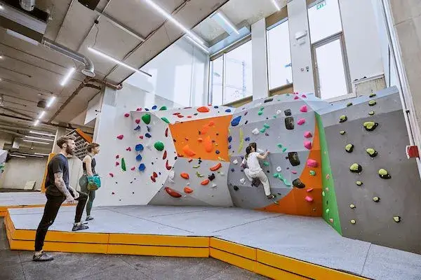 Image Inside London Fields Bouldering Gym Showing a Someone Climbing a Medium Sized Rock Wall as Two Others Watch